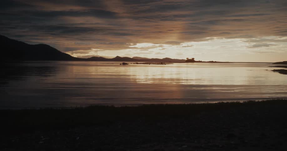 Sunset light reflecting on calm waters before the mountains