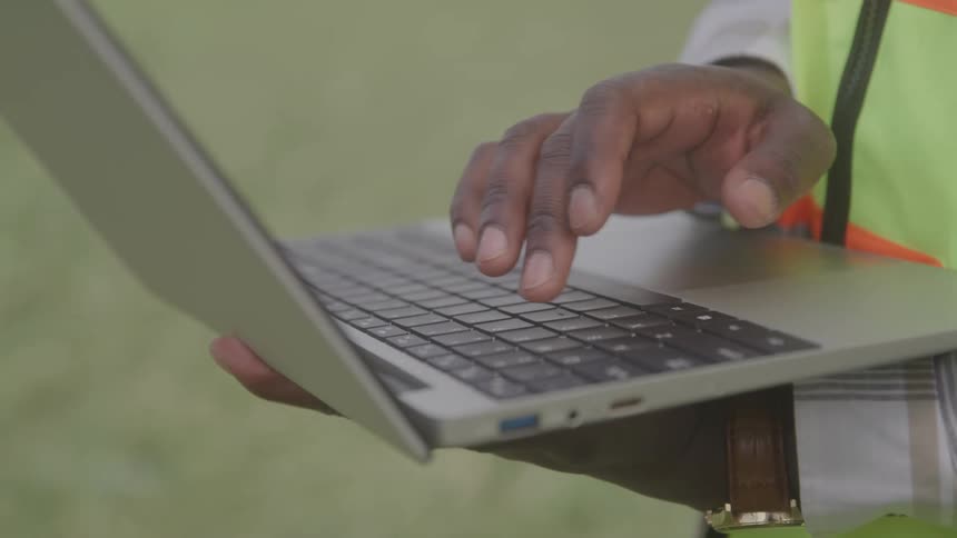 Construction worker holds a laptop computer and types with one hand