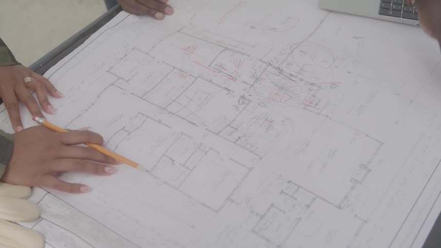 Hands mark up architectural blueprints with pencils