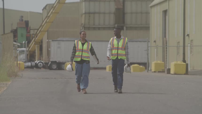 Two workers discuss while walking in an industrial area