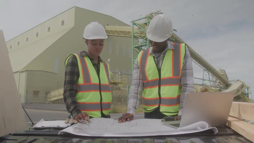 Two construction workers review blueprints at a worksite
