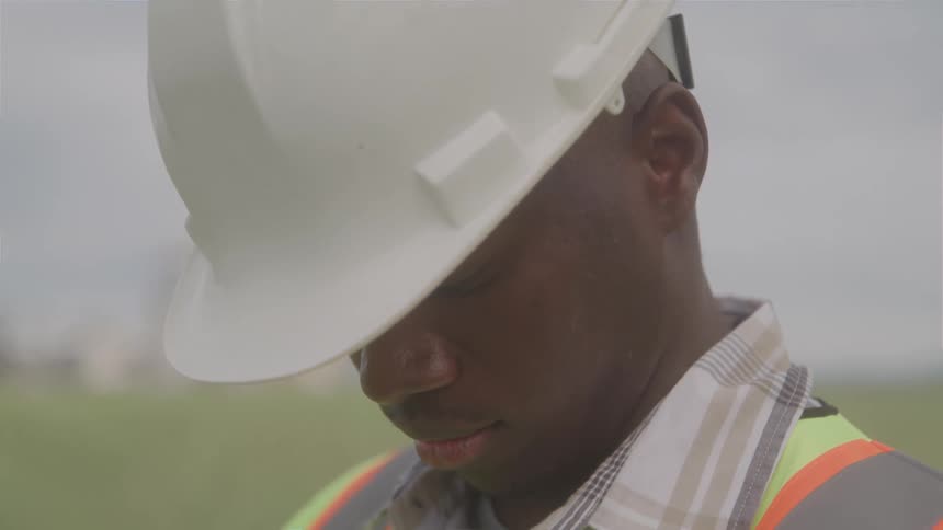 Worker wearing a helmet and reflective vest with closed eyes in an open field