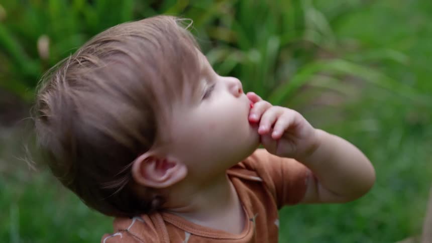 A toddler eats a berry and looks up to her mother in the garden