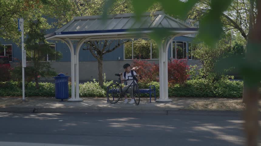 Person sitting at a bus stop holds a bicycle beside them