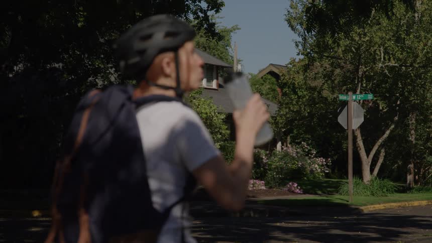 The woman is stopped on her bike drinking from a water bottle