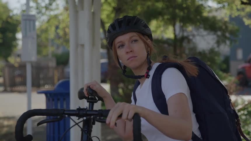 Cyclist with a backpack and helmet looking around while holding the bike