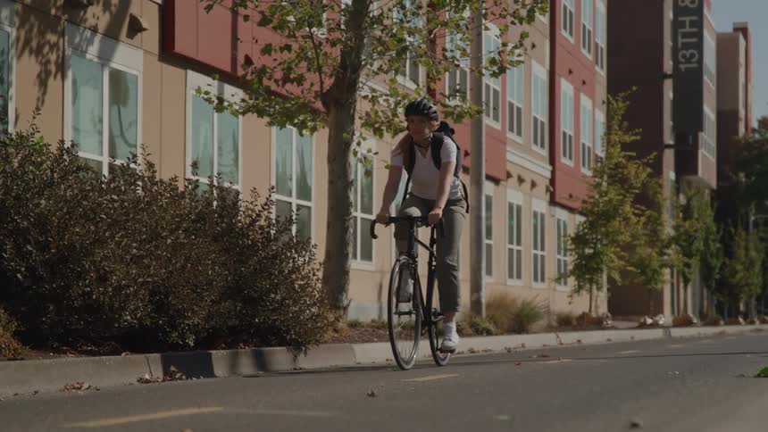 A person is riding a bicycle on a city street beside modern apartments