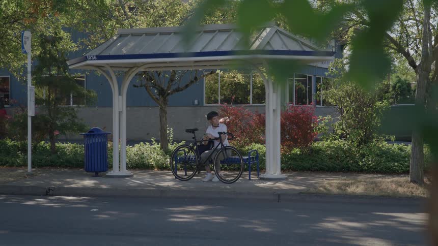 Cars pass by the cyclist sitting at the bus stop