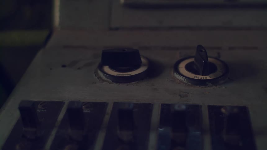 A close blurry view shows a piece of old machinery with a series of dark colored switches and knobs on a light colored panel