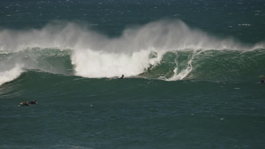 Surfers paddling in the ocean as large waves crash in the background