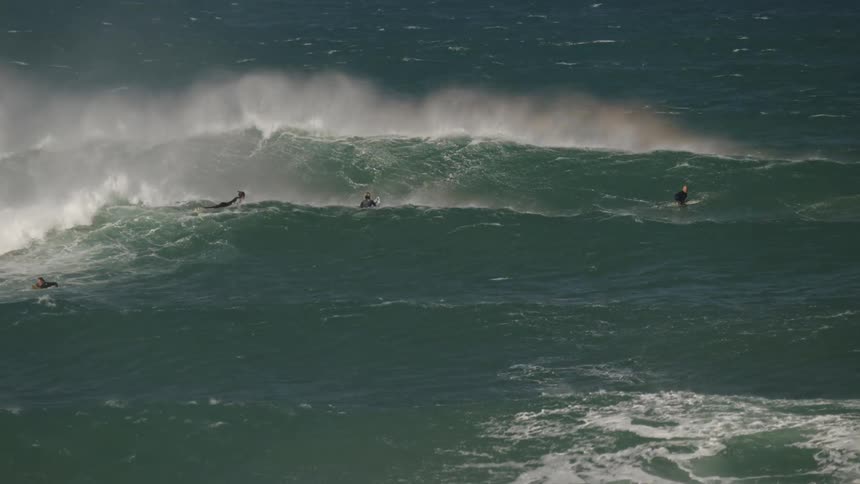 Based on the images from the video the scene is an aerial view of a person surfing on a large wave the surfer who is lying on their board is positioned near the crest of a breaking wave the ocean water is a deep blue and white foam is visible from th