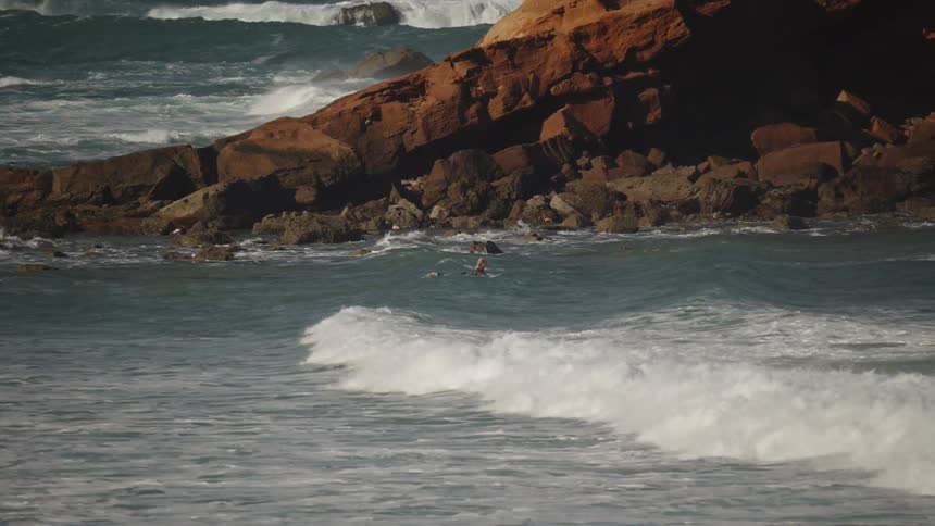 Based on the images from the video the scene is an aerial view of a person swimming in the ocean near a large rocky cliff face the person is wearing a dark wetsuit and is surrounded by waves crashing against the shore