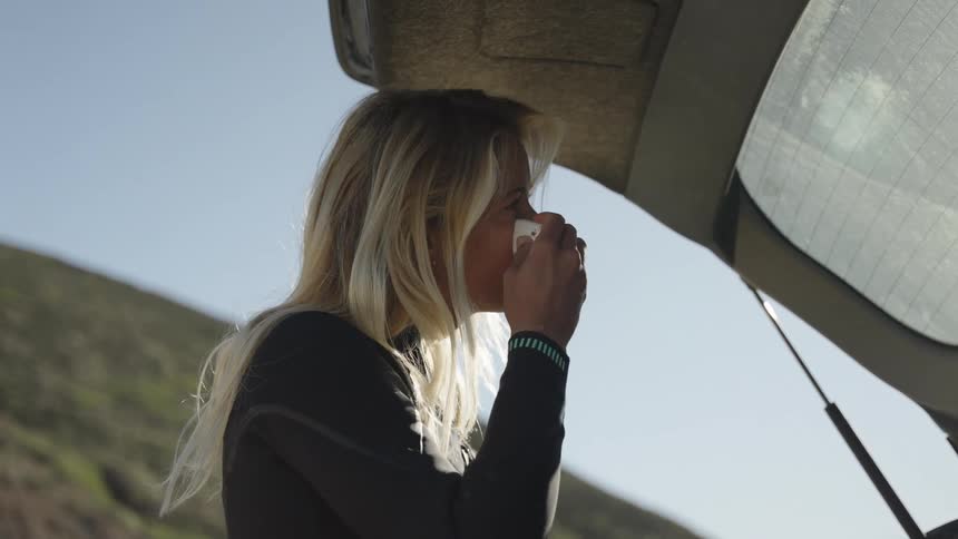 A blonde woman wearing a wet suit applies sunblock to her lips and face