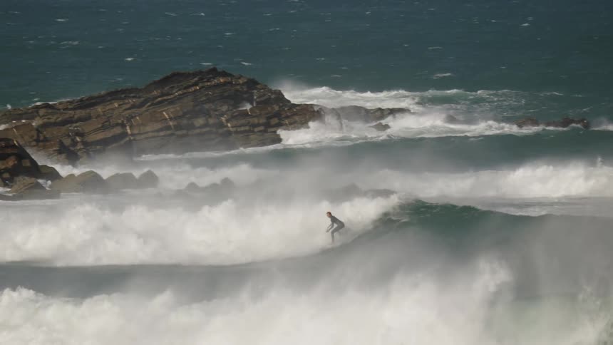 A surfer rides a wave near rocky shores