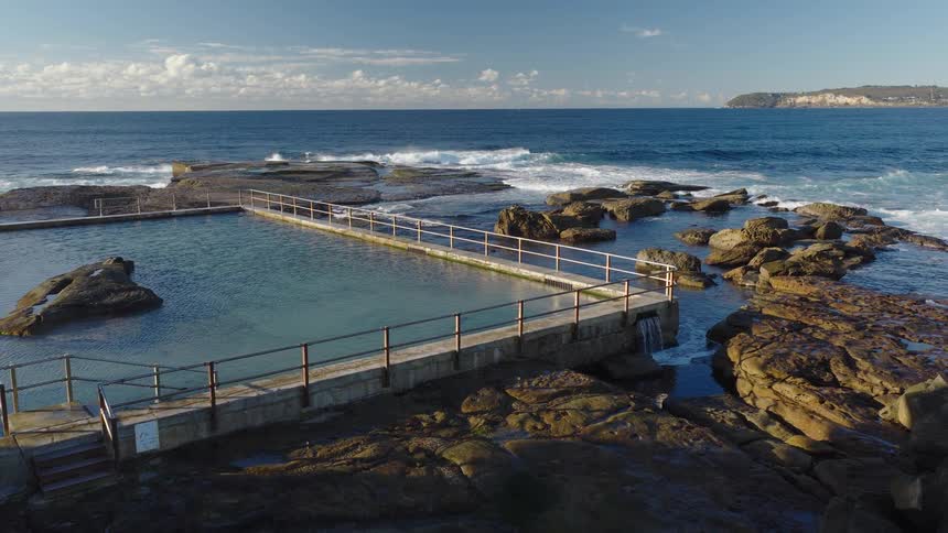 Natural seaside pool surrounded by rocks with waves in the background