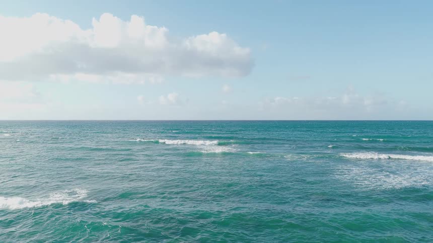 A fastmoving lowaltitude aerial shot flies rapidly over the surface of the open ocean under a blue sky with scattered clouds
