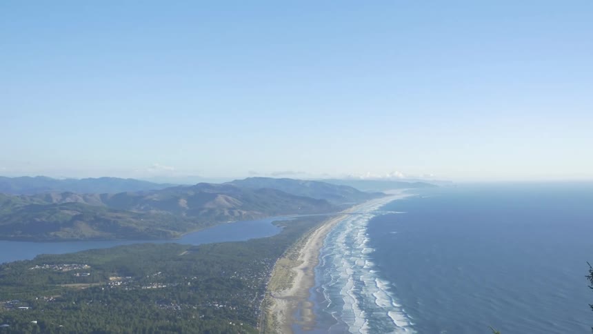 A long sandy beach with a clear blue sky and mountains on the left