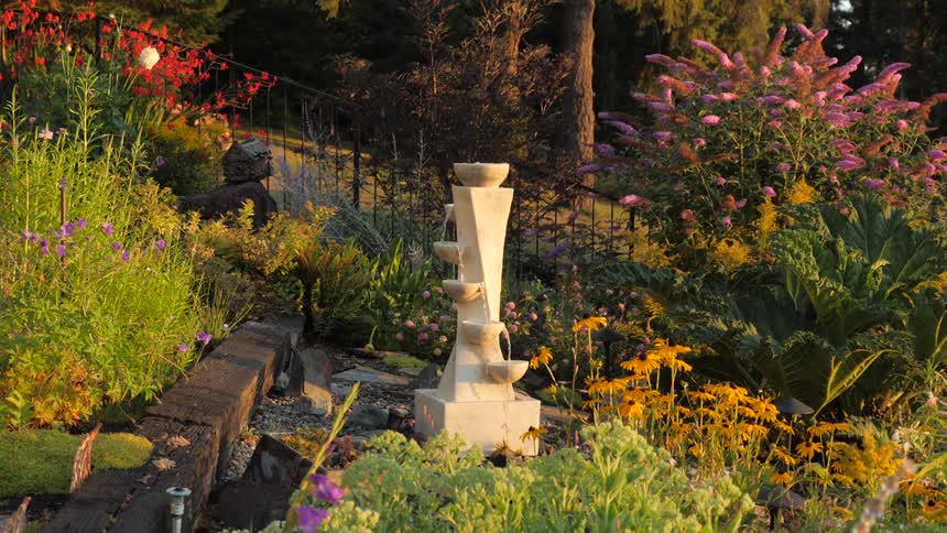Modern stone garden fountain with flowers in sunlight