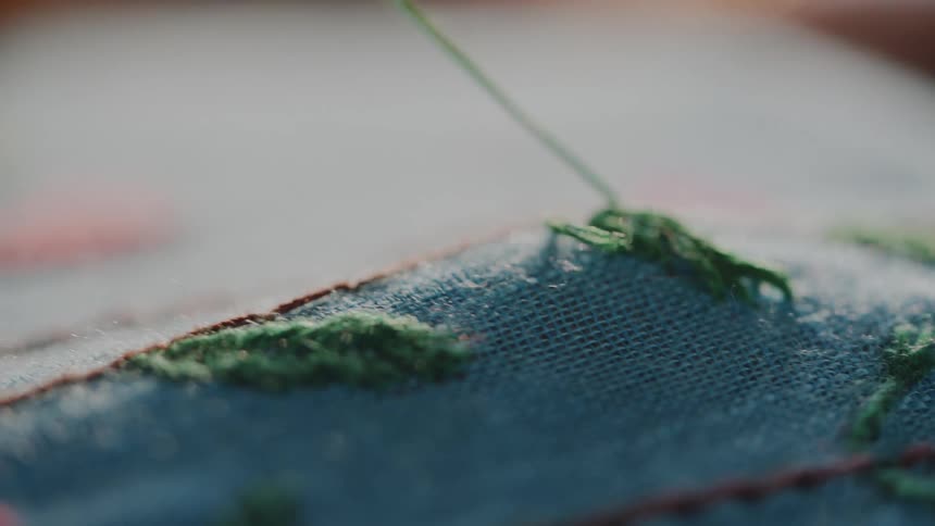 Hand embroidering blue fabric with green thread and colorful details