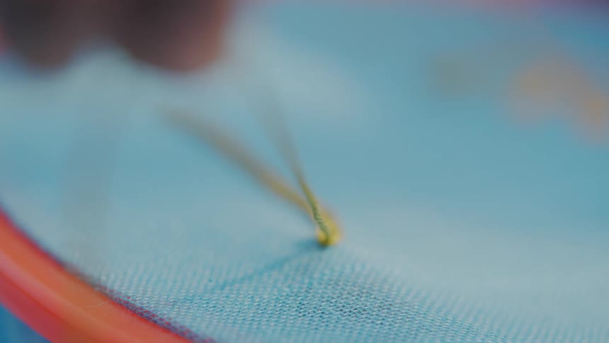 Hand embroidering blue fabric with yellow thread in a hoop