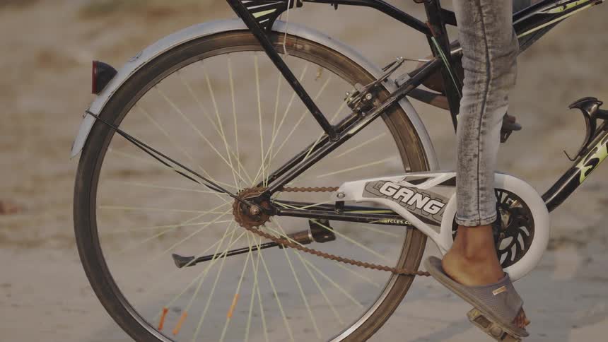 A person wearing sandals pedals a bicycle over a dirt path