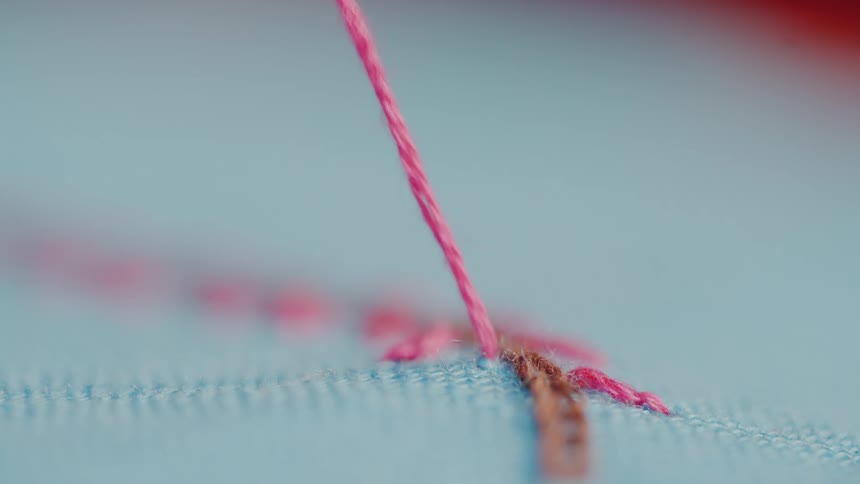 Pink thread being stitched into blue fabric