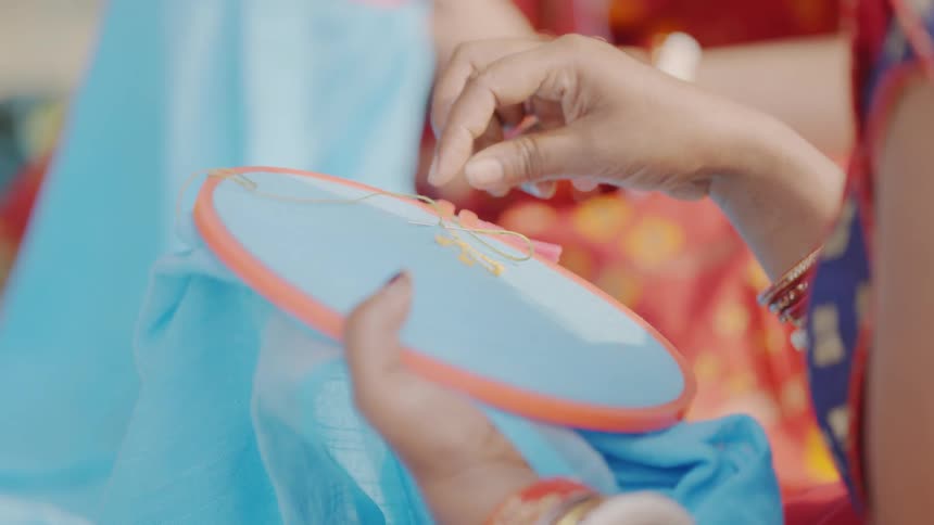 Female hands embroider on blue fabric held in an embroidery hoop
