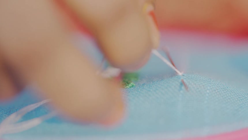 Macro of stitching as a needle pulls white thread through blue fabric
