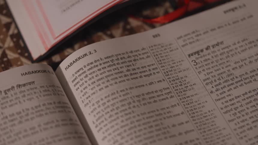 A large book is open to a page with black text in yiddish surrounded by other texts and papers