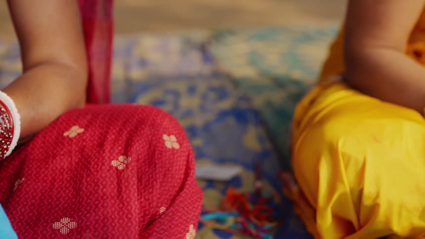 Hands work on colorful embroidery over blue fabric stretched in a hoop