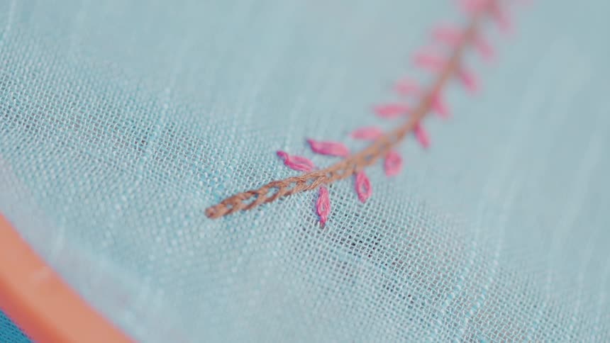 A closeup shot of a persons hands and a needle performing embroidery on a light blue fabric