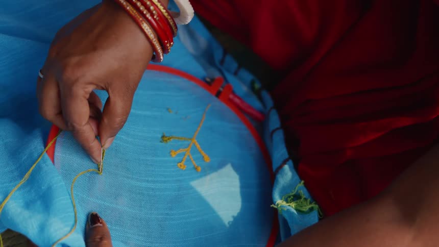 Hands embroidering blue fabric with yellow thread in a hoop