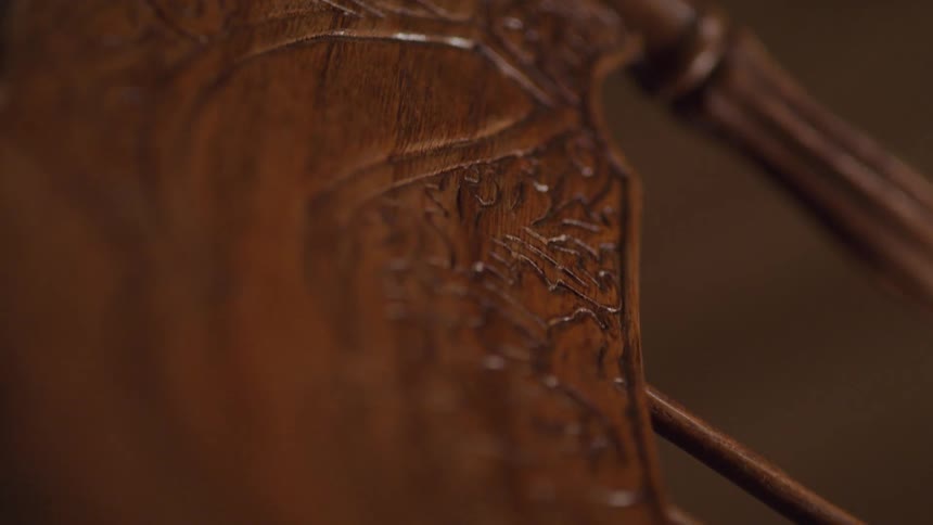 A close angled view shows the back of a dark brown wooden chair with a carved ornate design on its surface