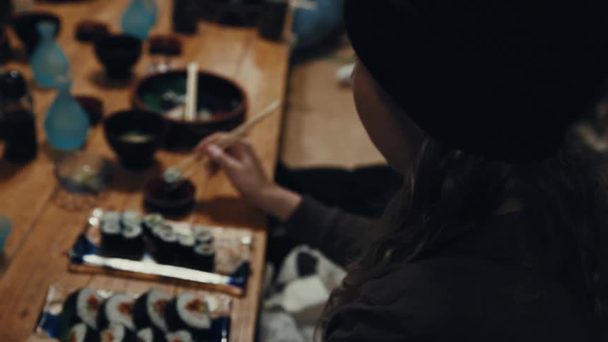 Person using chopsticks while eating sushi at a wooden table