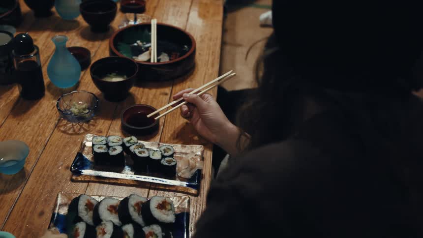 People sitting at a short table with their legs crossed eating sushi rolls with chopsticks