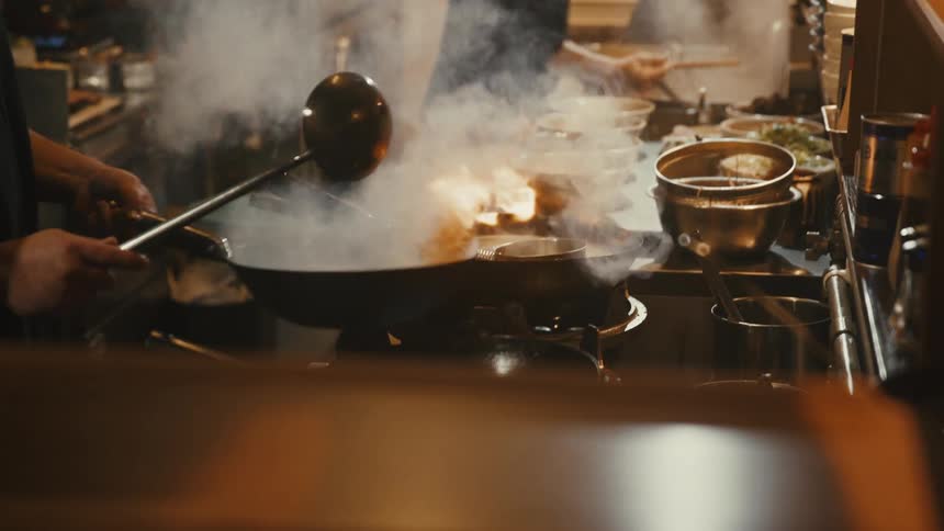 Chef tossing food in a steaming wok inside a busy kitchen