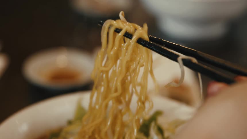Chopsticks lifting noodles from a bowl of ramen