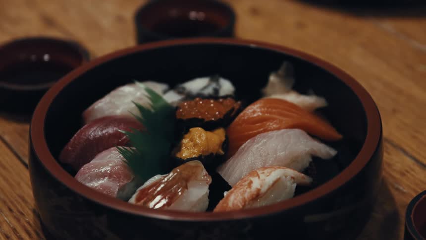 A bowl of assorted sushi sits on a wooden table