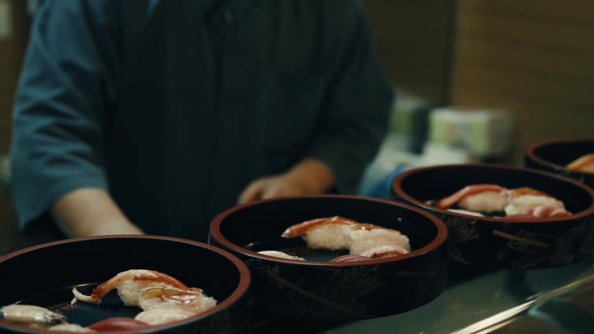 A chef presents sushi plates on restaurant counter