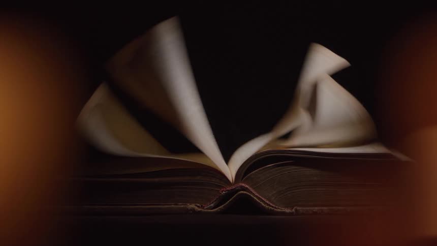 Based on the images from the video an open book with blank pages is shown on a table in a dimly lit room the pages are fluttering as if from a gentle breeze