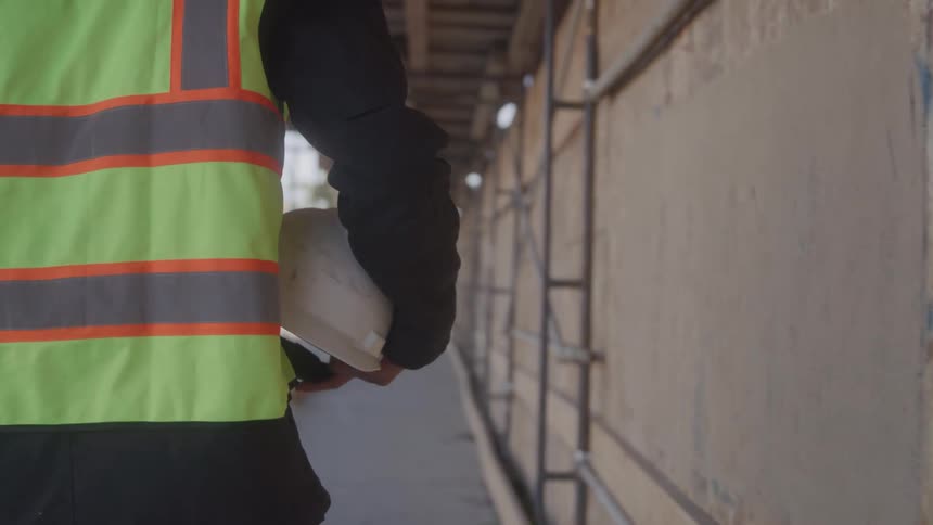 The worker carries his hard hat under the scaffolding