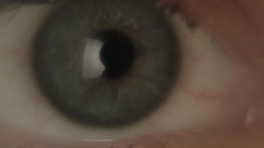 Based on the images from the video a closeup shot of a lightcolored human eye is shown with the eyelid blinking open and shut the iris of the eye is a mix of green and gray tones