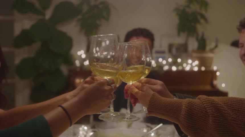 People toast with wine at a cozy dinner with twinkling lights