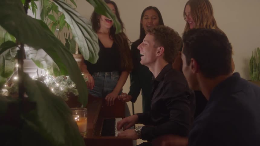 Man plays piano while friends gather smiling around