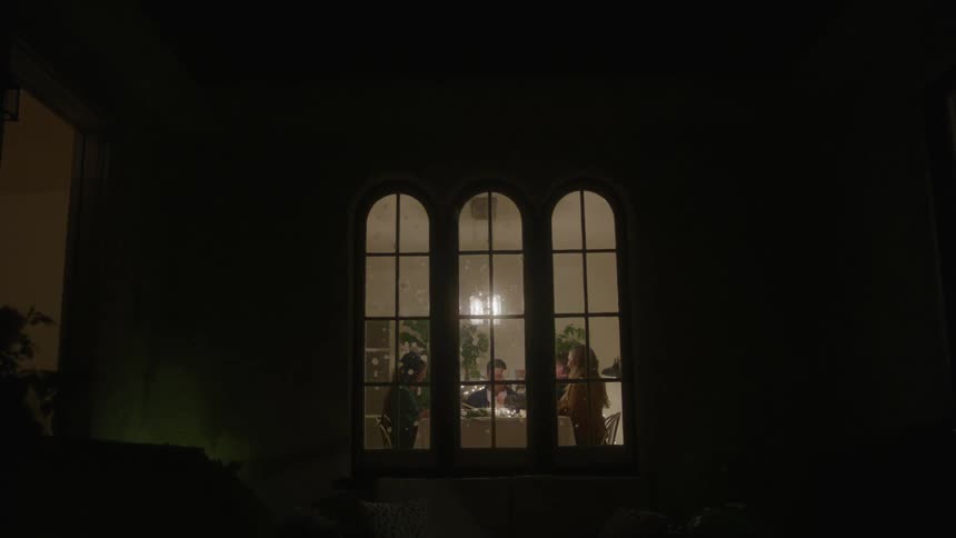A group of people has dinner next to a window split in three sections