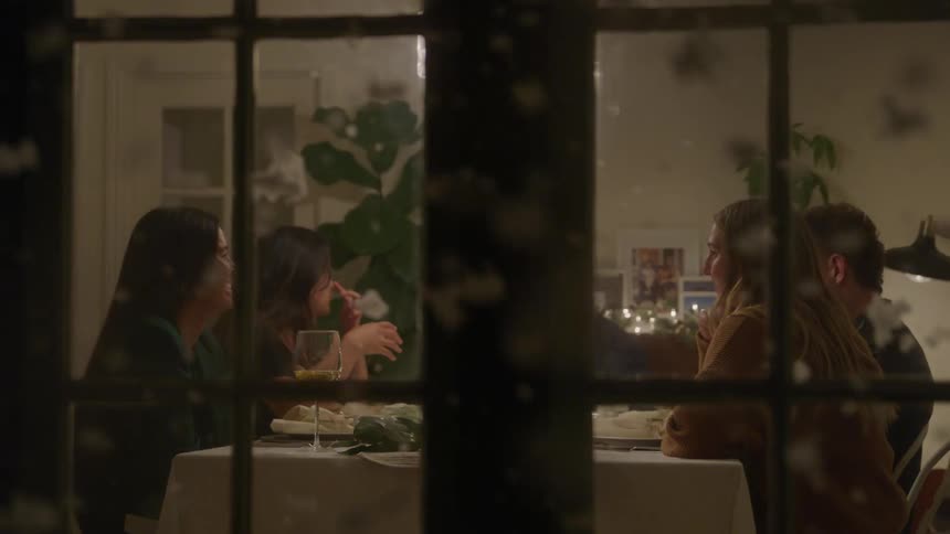Based on the video a group of people is gathered at a dining table seen through a glass door or window the scene is dimly lit with candles and other lights on the table creating a warm and cozy atmosphere