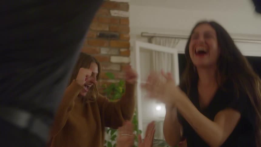 A group of friends is laughing and celebrating in a home yelling raising their arms in the air laughing and jumping in excitement