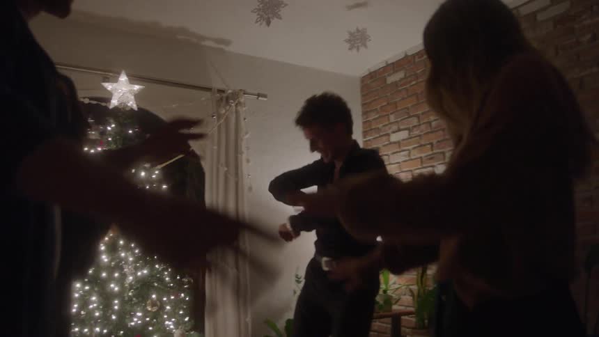 Closeup of people dancing beside a sparkling christmas tree at night