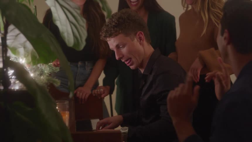 Man playing the piano while a group of people sings around him