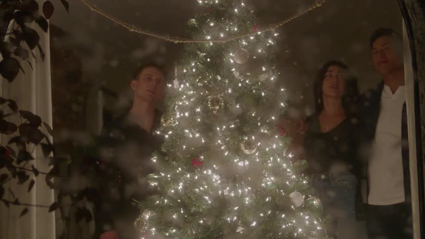 People singing around a decorated christmas tree indoors